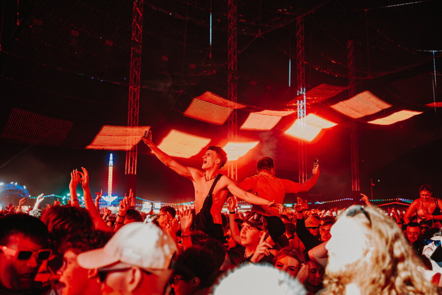 customer sitting on their friends shoulders under the orange lights of chevron stage at Leeds Festival 